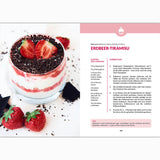 Eine Rezeptseite aus dem Fettverlust Fibel Kochbuch zeigt Erdbeer-Tiramisu in einem Glas, geschichtet mit Sahne, Erdbeeren und Schokoladenraspeln, daneben frische Erdbeeren auf einer weißen Fläche.