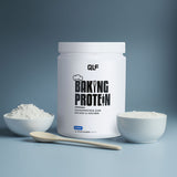 Ein weißer Behälter mit der Aufschrift Baking Protein steht auf einer blauen Fläche, umgeben von Schalen mit Pulver und Sahne sowie einem Holzlöffel - perfekt für Fitnessrezepte mit idealer Konsistenz. Der blaue Hintergrund ergänzt die Szene.