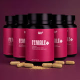 Fünf schwarze Dosen Female+ mit rosafarbenen Etiketten und gelben Kapseln sind vor einem weinroten Hintergrund mit Farbverlauf verteilt. Female+ unterstützt den Energiestoffwechsel, fördert eine gesunde Haut und enthält 90 Kapseln pro Flasche.