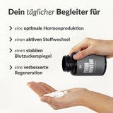 Eine Person schüttet weiße Kapseln aus einer schwarzen Fundamentum-Flasche in ihre Hand. Deutscher Text fördert wissenschaftlich basierte Nahrungsergänzung für optimale Hormonproduktion, aktiven Stoffwechsel und Gesundheit optimieren.