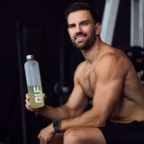Sportlicher Mann mit QLF Hydration Shaker (100% off) in Hand sitzt im Fitnessstudio und lächelt in Kamera