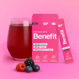 Ein Glas mit einem roten Getränk steht neben einer rosafarbenen Benefit Energy Box und einem Beutel mit der Hydration-Formel. Vorne sind gemischte Beeren zu sehen, und die Verpackung zeigt Fakten und Symbole zur Nahrungsergänzung auf einem leuchtend rosa Hintergrund.