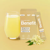 Ein Glas mit einem gelben Getränk steht neben einer Benefit Hydration Box und einem Beutel, daneben Holunderblüten. Auf der Verpackung sind das Elektrolyt-Formel, Magnesium und Vitamine vor einem hellgelben Hintergrund abgebildet.