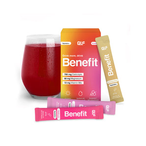 Ein Glas mit rotem Getränk steht neben der Benefit Hydration Probebox, die Informationen zu Elektrolyt-Formel, Magnesium und Vitaminmischungen enthält; davor befinden sich drei rosa und golden verpackte Hydration-Stick Getränkepulver.