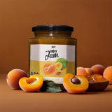 Ein Glas Tasty Jam Aprikose mit 80% Fruchtanteil steht auf einer braunen Fläche, umgeben von frischen ganzen und halbierten Aprikosen. Das Etikett zeigt Aprikosen und das Wort "Aprikose".