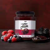 Ein Glas Tasty Jam mit der Aufschrift Waldbeere ist mit frischen Himbeeren, Heidelbeeren und Brombeeren abgebildet. Dieser kalorienarme Fruchtaufstrich besteht zu 80 % aus Früchten und ist eine köstliche Marmeladenalternative, die vor einem dunklen Hintergrund präsentiert wird.