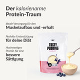 Auf der Verpackung eines proteinreichen Puddings mit der Aufschrift "Eiweiß" befindet sich ein Löffel Pudding mit Heidelbeeren. Der deutsche Text wirbt für Eiweiß zum Muskelaufbau, zur Unterstützung von Diäten und für eine lang anhaltende Sättigung.