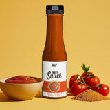 Eine Flasche Tasty Sauce Curry-Ketchup steht auf einer gelben Fläche neben einer Schüssel mit Ketchup, frischen Tomaten und Currypulver - ideal als kalorienarme Diät-Zutat vor dem leuchtend gelben Hintergrund.