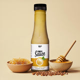Eine Flasche Tasty Sauce Honigsenf steht zwischen Honigwaben und einer Schale mit einem Honiglöffel, umgeben von Senfkörnern - eine ideale kalorienarme Diät-Zutat auf einem beigen Hintergrund.