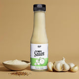 Eine Flasche Tasty Sauce Knoblauchsauce steht aufrecht mit einem Etikett, auf dem Knoblauchzwiebeln abgebildet sind. Daneben befindet sich eine Schale mit Soße, Knoblauchzehen und Gewürzen, die diese kalorienarme Diätzutat vor einem schlichten beigen Hintergrund hervorhebt.
