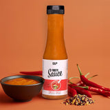 Eine Flasche Tasty Sauce steht auf einer orangefarbenen Fläche neben einer Schale mit Sauce, Chiliflocken und ganzen roten Chilischoten vor einem orangefarbenen Hintergrund.