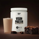 Ein Becher veganes Proteinpulver mit der Aufschrift Schokolade Brownie steht neben einem Glas veganen Proteinshake und einem reichhaltigen Schokoladen-Brownie vor einem dunklen Hintergrund - perfekt für Ihre eigene vegane Revolution.