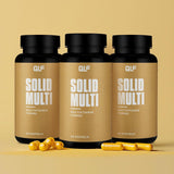 Drei Dosen Solid Multi stehen vor beigem Hintergrund, davor liegen mehrere gelbe Kapseln. Jede Dose enthält 60 Multivitamin-Kapseln mit natürlichen Vitaminen und Coenzym Q10.