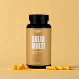 Eine schwarze Dose mit der Aufschrift Solid Multi steht aufrecht auf einer gelben Fläche, umgeben von gelben Kapseln. Der monochromatische gelbe Hintergrund unterstreicht die lebendige und gesundheitsfördernde Wirkung von Solid Multi.