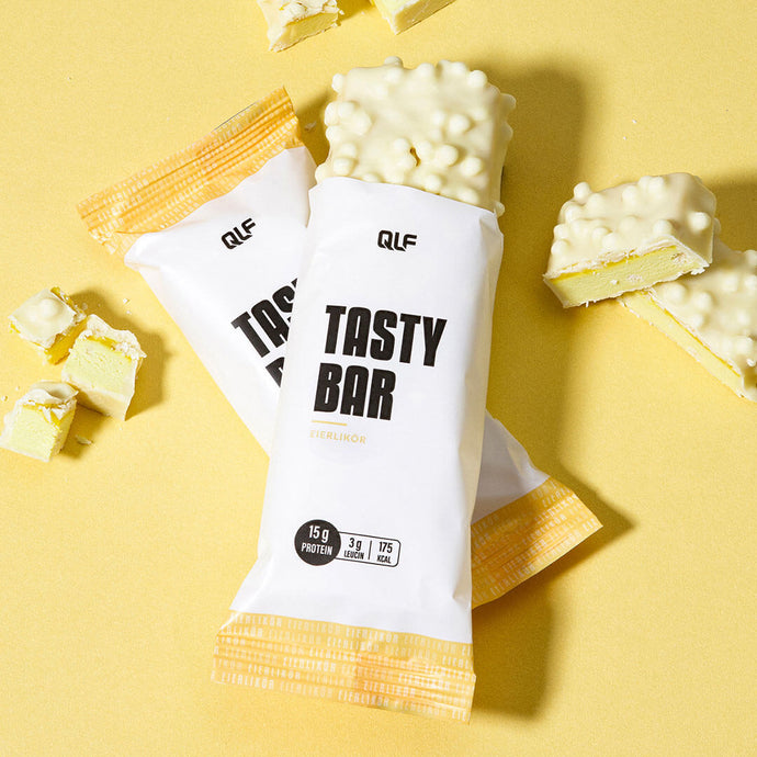 Ein teilweise ausgepackter, mit weißer Schokolade überzogener Tasty Bar liegt auf einer gelben Fläche, neben der sich ein weiterer eingepackter Riegel und Bruchstücke befinden - der perfekte kalorienarme Snack für Ihr Fitnessprogramm.