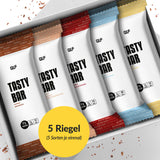 Eine Schachtel mit fünf sortierten Tasty Bar Proteinriegeln, jeder in einer einzigartigen Farbverpackung. Auf einem gelben Etikett steht "5 Riegel (5 Sorten je einmal)". Perfekt als kalorienarmer Snack für Fitness-Fans!.